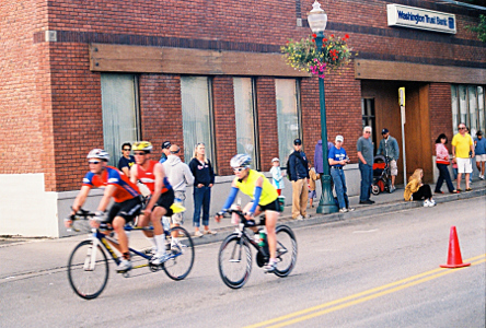 [Two bikes are heading down the road to the left. One bike has a cyclist with a yellow shirt. The other bike is one with two sets of pedals and two riders. Both bikes are a bit blurred in the image as they zipped along.]